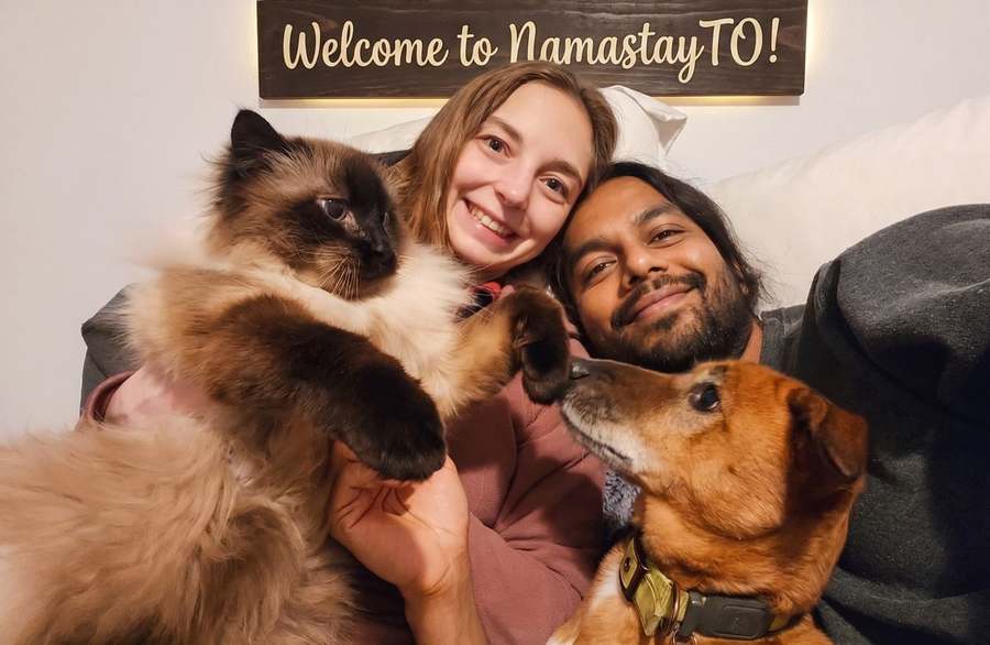 Emilee and Pranay with Oliver the cat and Kumbah the dog under a Welcome to NamastayTO sign